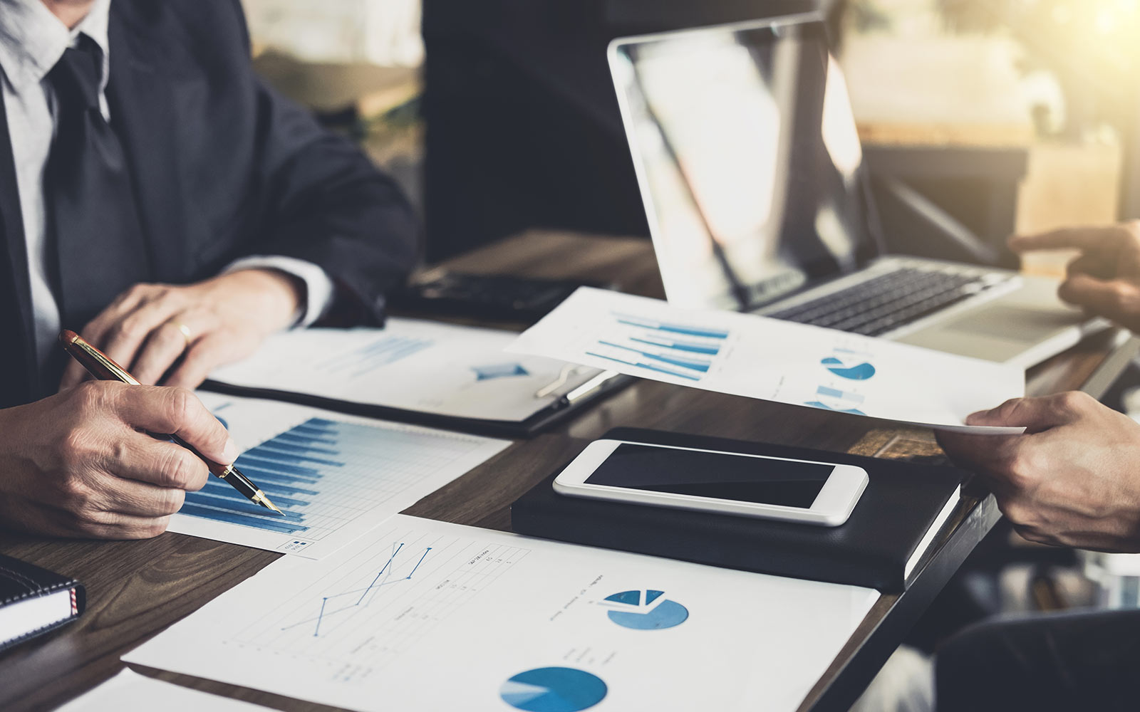 Close-up of a table full of a laptop and paperwork with two people discussing the documents