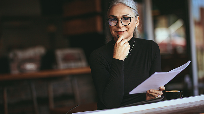 Woman smiling and holding paperwork in one hand and a pen in the other