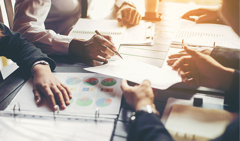 Close-up of a table with binders open with documents inside and four people around it