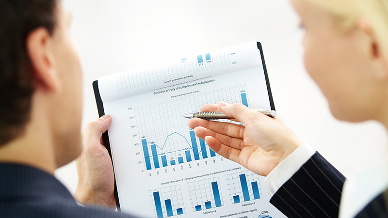 Close up of two people discussing a bar graph on a clipboard