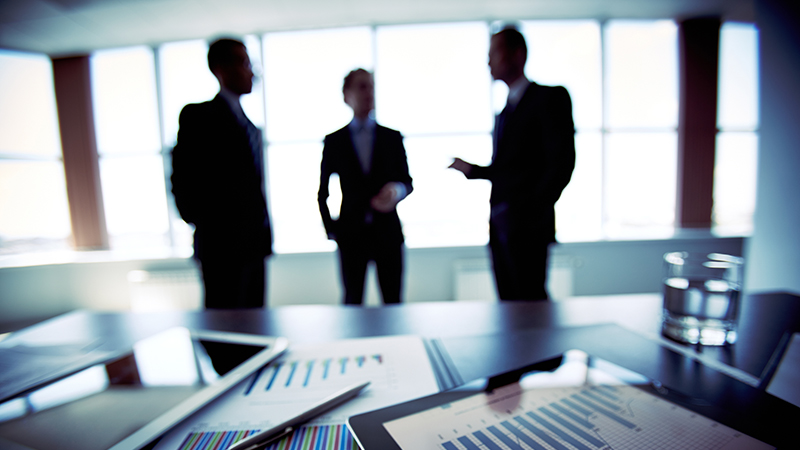 Three businessmen in a standing discussion by office window