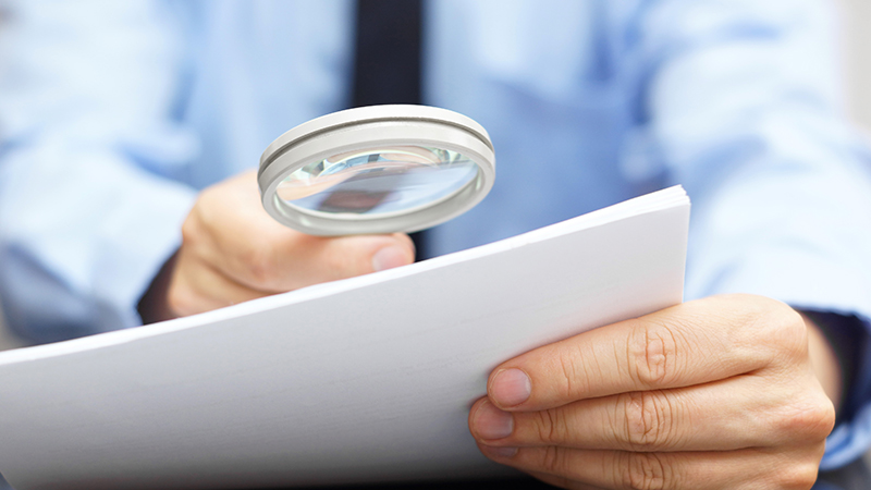 Hand holding magnifying glass over document