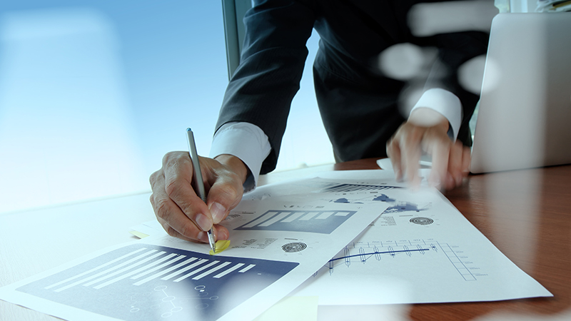 Businessman writing on printed graphs with pen